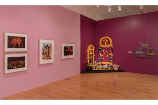 Exhibiting items: A Traditional altar, Photographs, and mixed media pieces displayed in a pink gallery room.