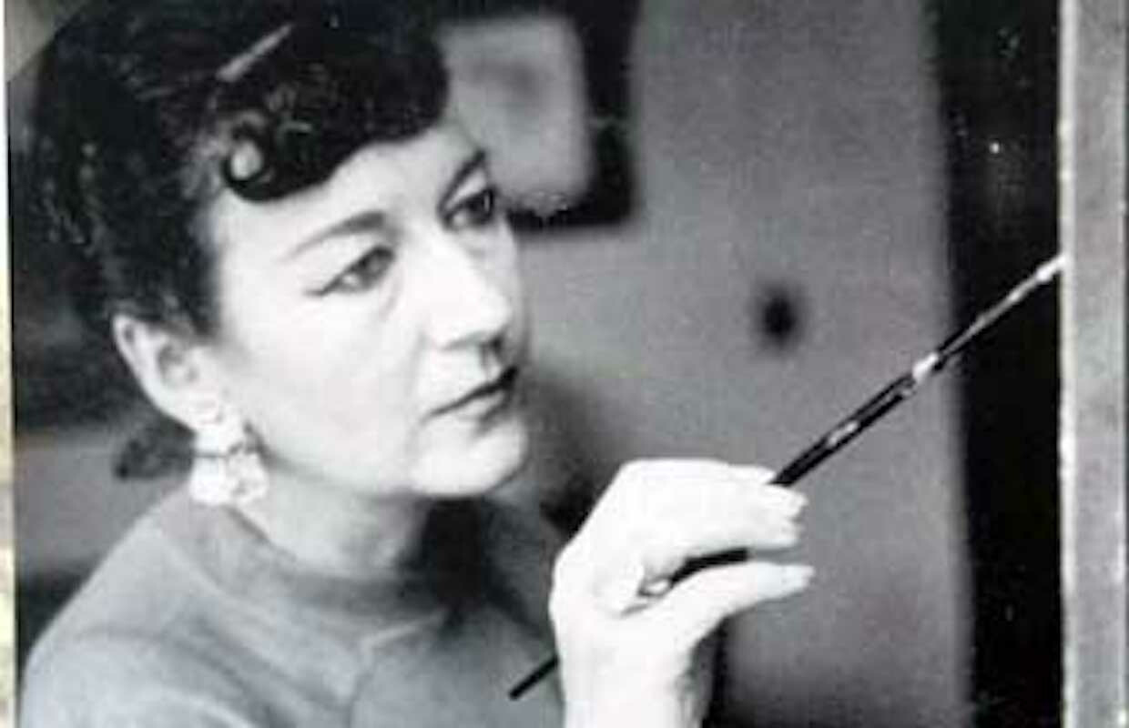 A woman holds a paint brush to a surface