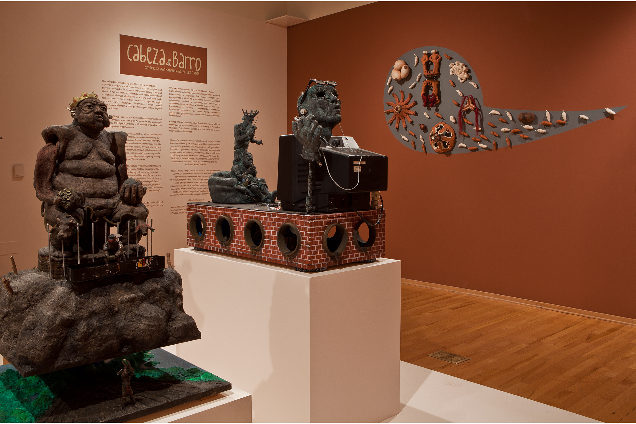 3-D art in gallery with exhibit opening text in the background.