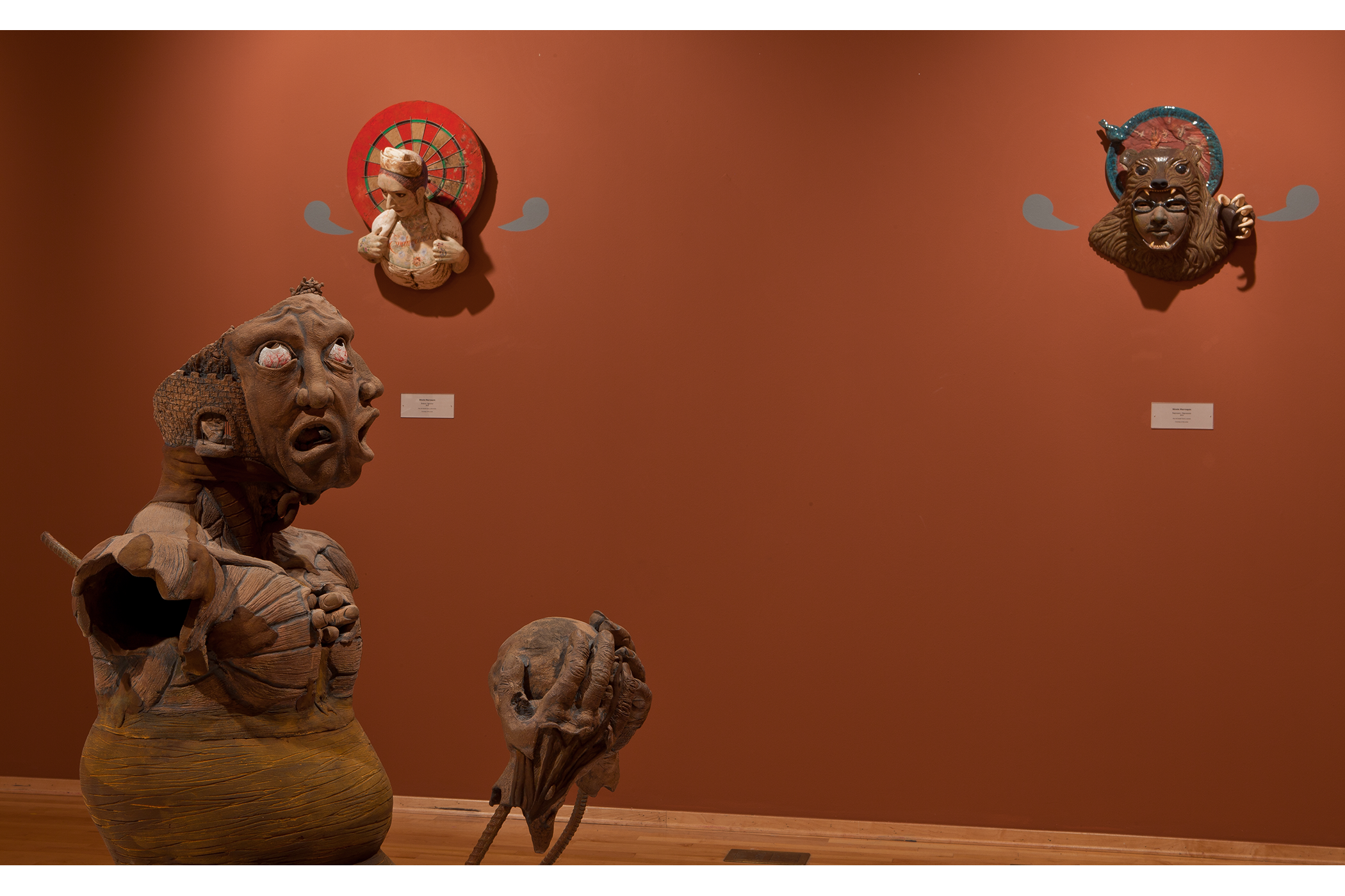Foreground sculpture: a figure with three  different heads attached to a morphed body.