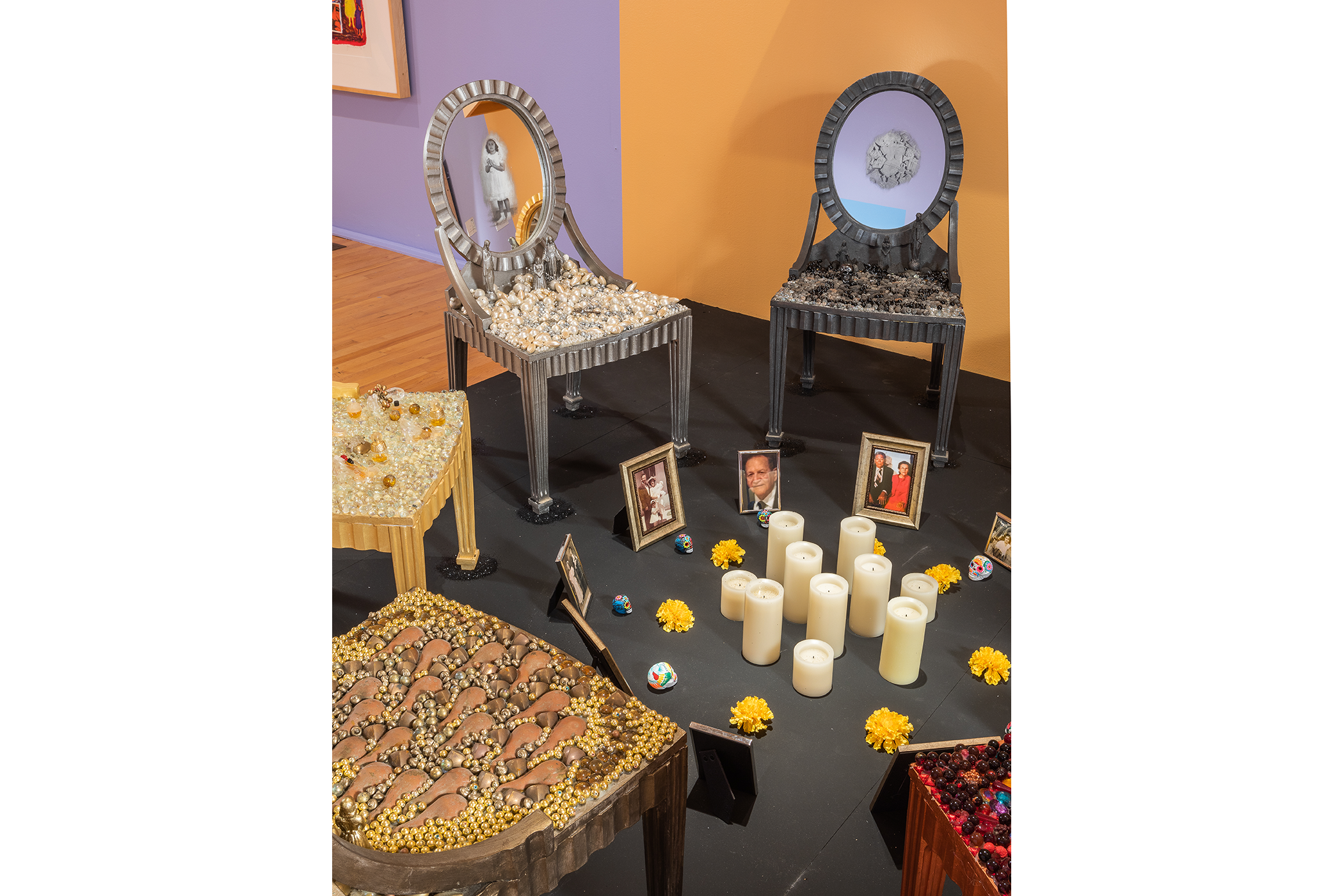 A long view of the chair installationfeaturing the chairs, a few picture frames arranged into a circle with ten candles, marigolds, and sugar skulls in the center.