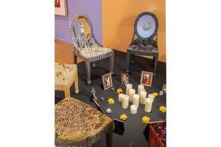 A long view of the chair installationfeaturing the chairs, a few picture frames arranged into a circle with ten candles, marigolds, and sugar skulls in the center.