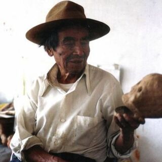 A man in a brimmed hat holds a paper mache skulls in his hand