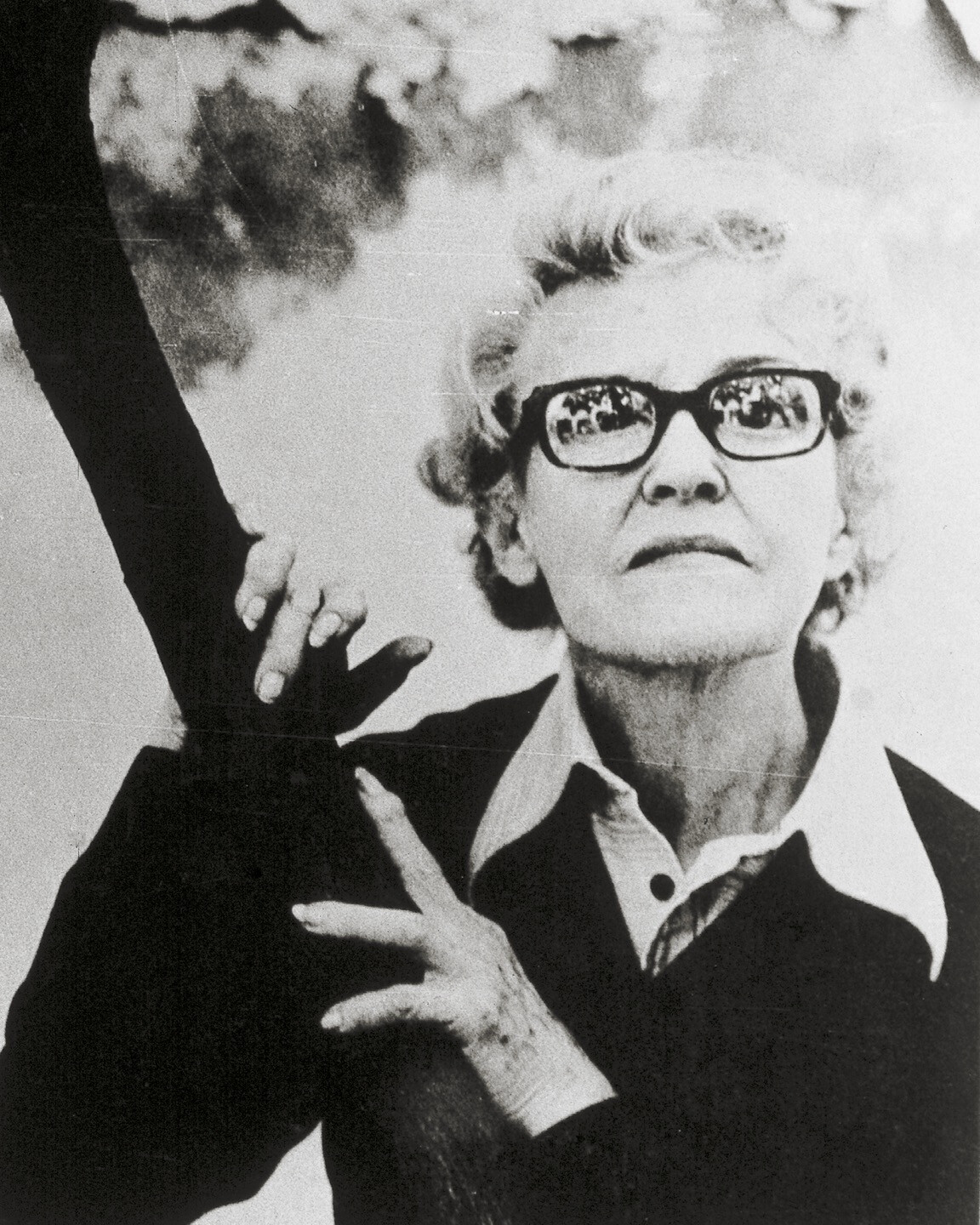 A woman with glasses leans on a branch