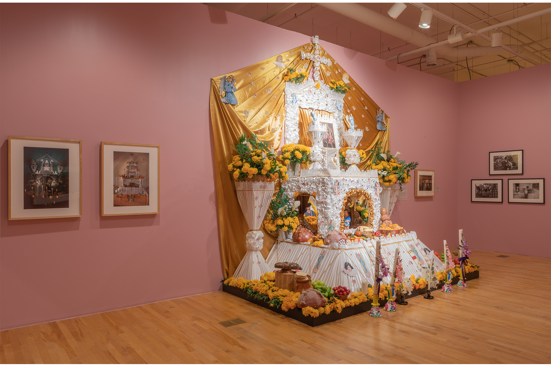 A white ofrenda with a golden fabric backdrop, decorative with references to Mexica culture and Catholic traditions.