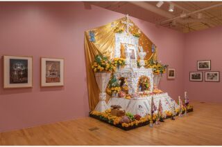 A white ofrenda with a golden fabric backdrop, decorative with references to Mexica culture and Catholic traditions.