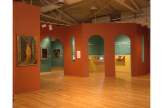 Image of gallery. Orange and teal walls visible with pieces of Remedios Varo's art