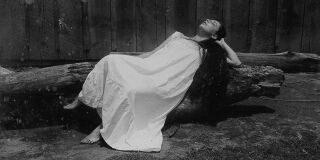 Black and white photo of woman in white dress reclining on wooden log