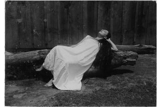 Black and white photo of woman in white dress reclining on wooden log