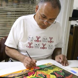 A seated man wearing glasses paints with a brush