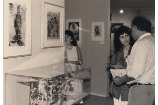 Black and white photograph of artist talking with a man at the exhibit