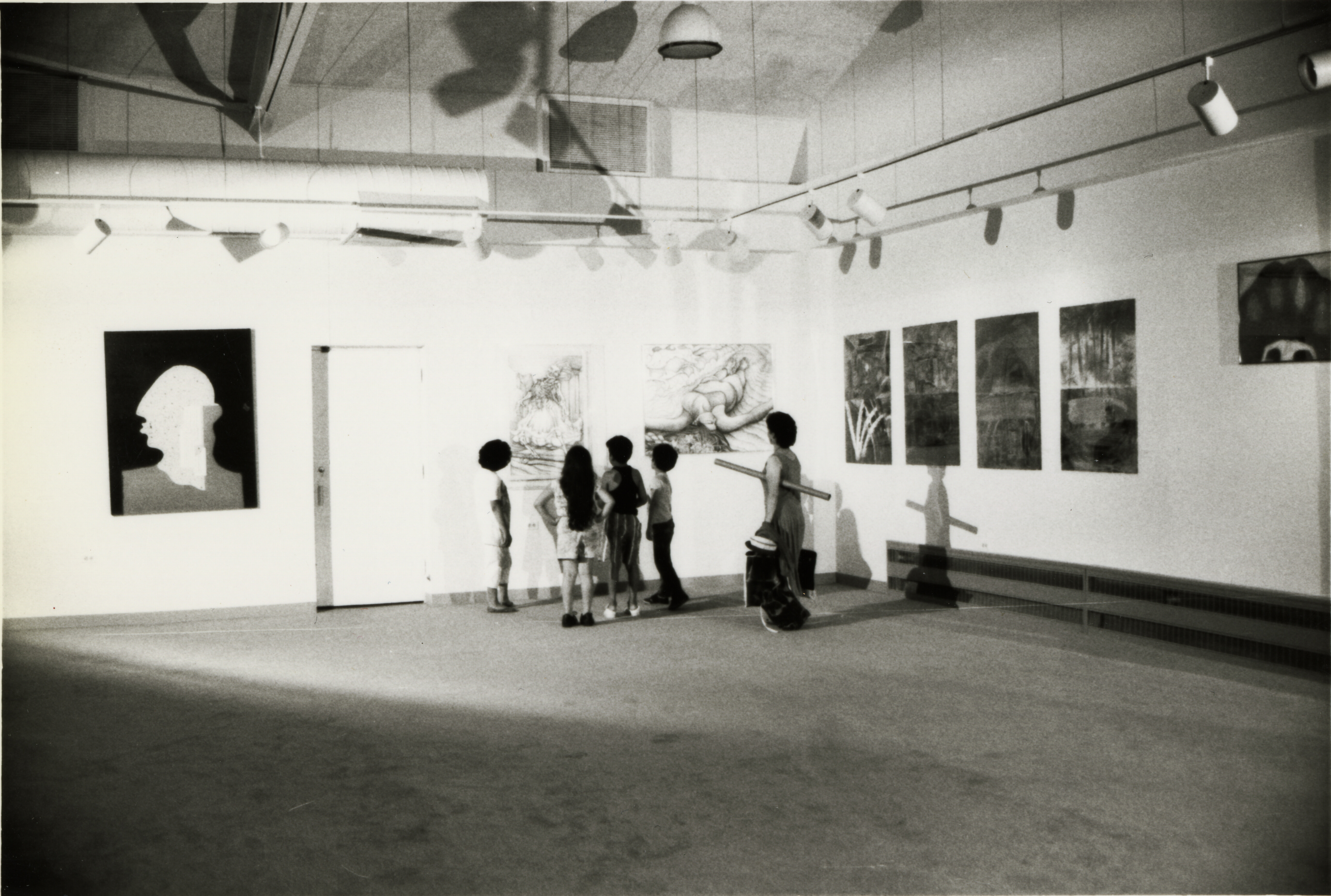 Black and white photograph of four children and adult looking at art in gallery