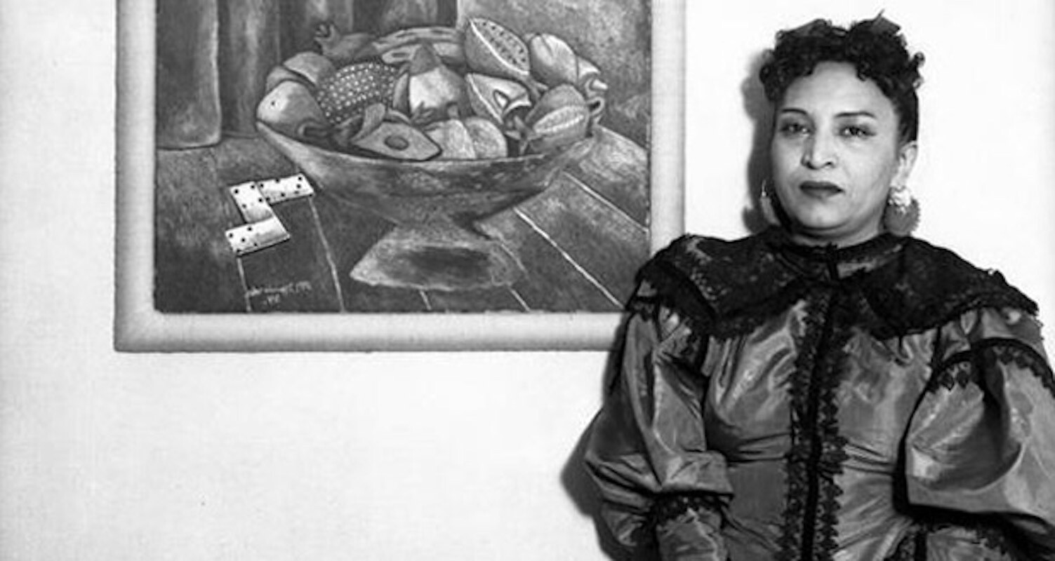 A woman in an elaborate dress poses next to a painting