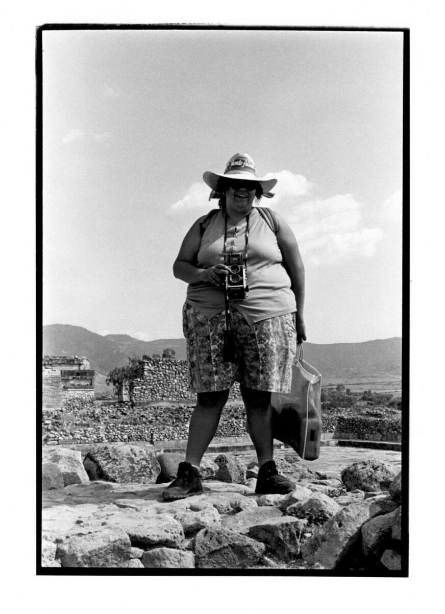 A woman wearing a hat and holding a camera stands for a photo in the desert