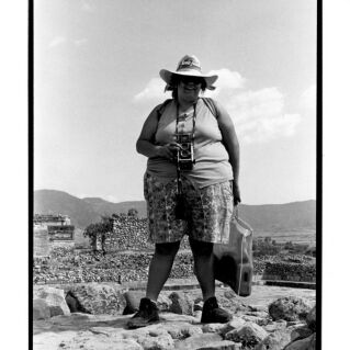 A woman wearing a hat and holding a camera stands for a photo in the desert