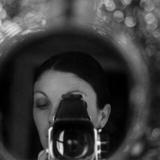 A woman with a large brimmed hat takes a photo of her self in a reflection