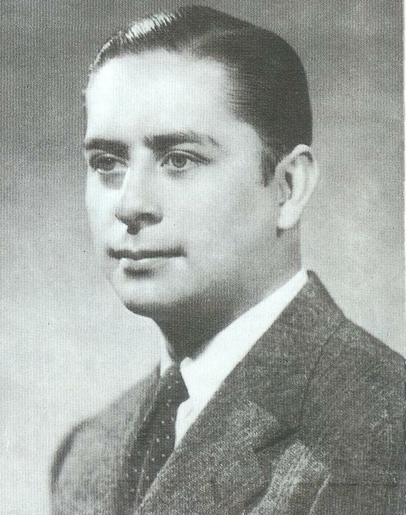 A man in a suit poses for a photo in black and white