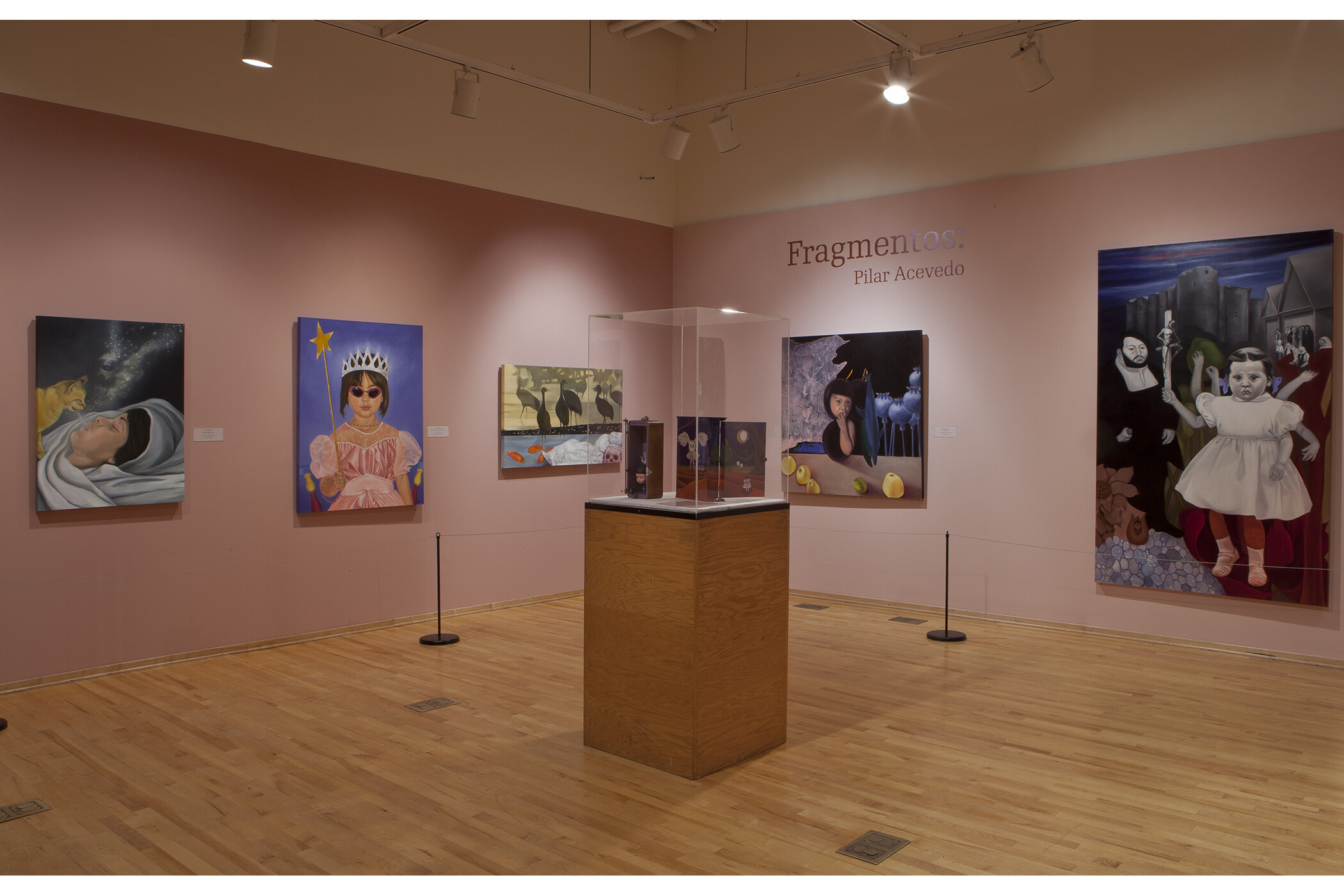two gallery walls, artwork hanging, with a glass case in the center of the room.