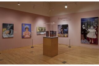 two gallery walls, artwork hanging, with a glass case in the center of the room.