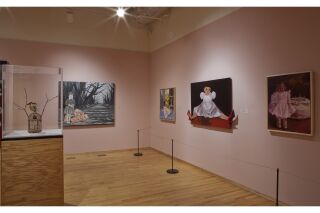 three fourths view of the gallery space, five paintings hang on the wall with two glass cases in the center.