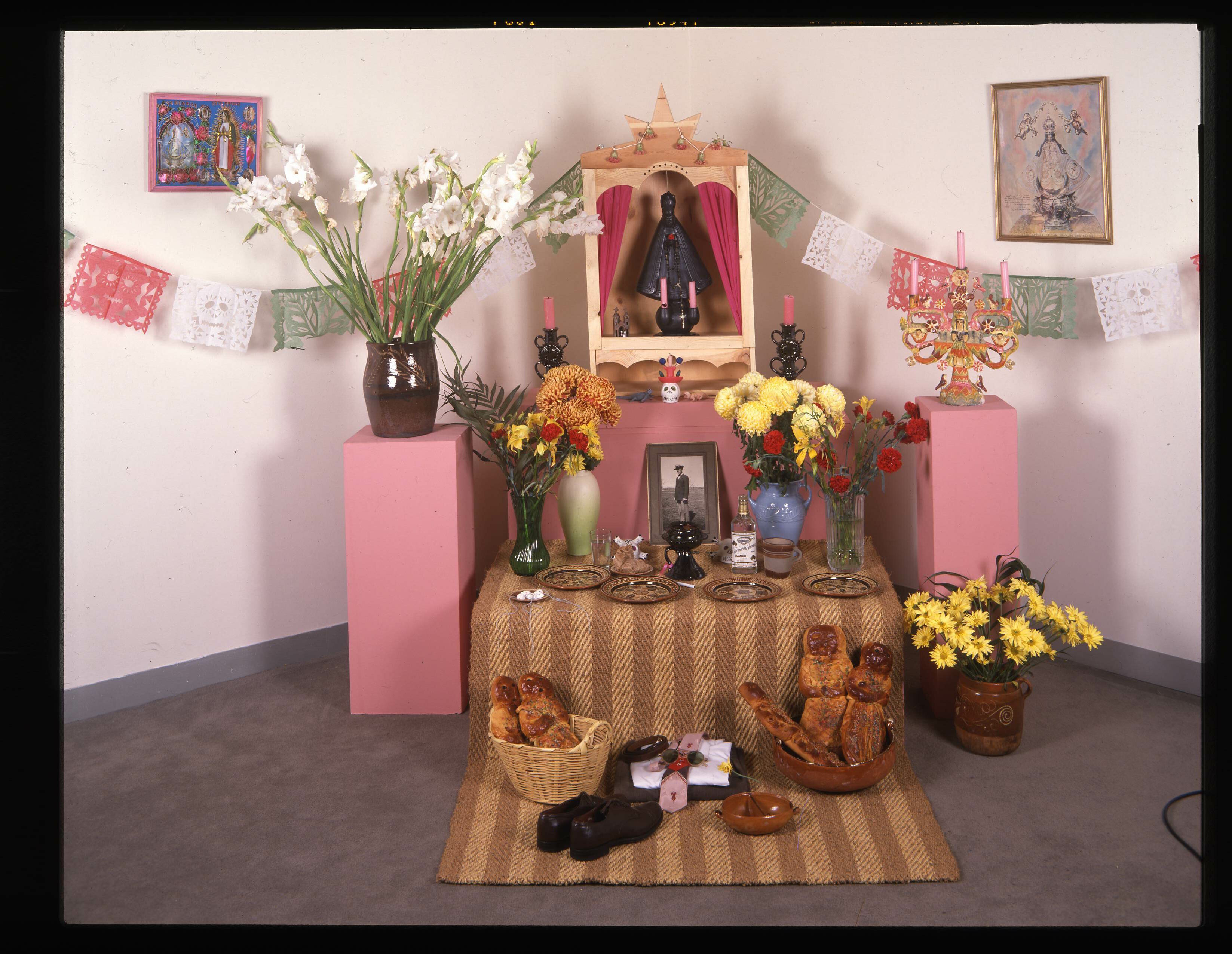 Ofrenda including hanging art, flowers, and a statue of the Virgen