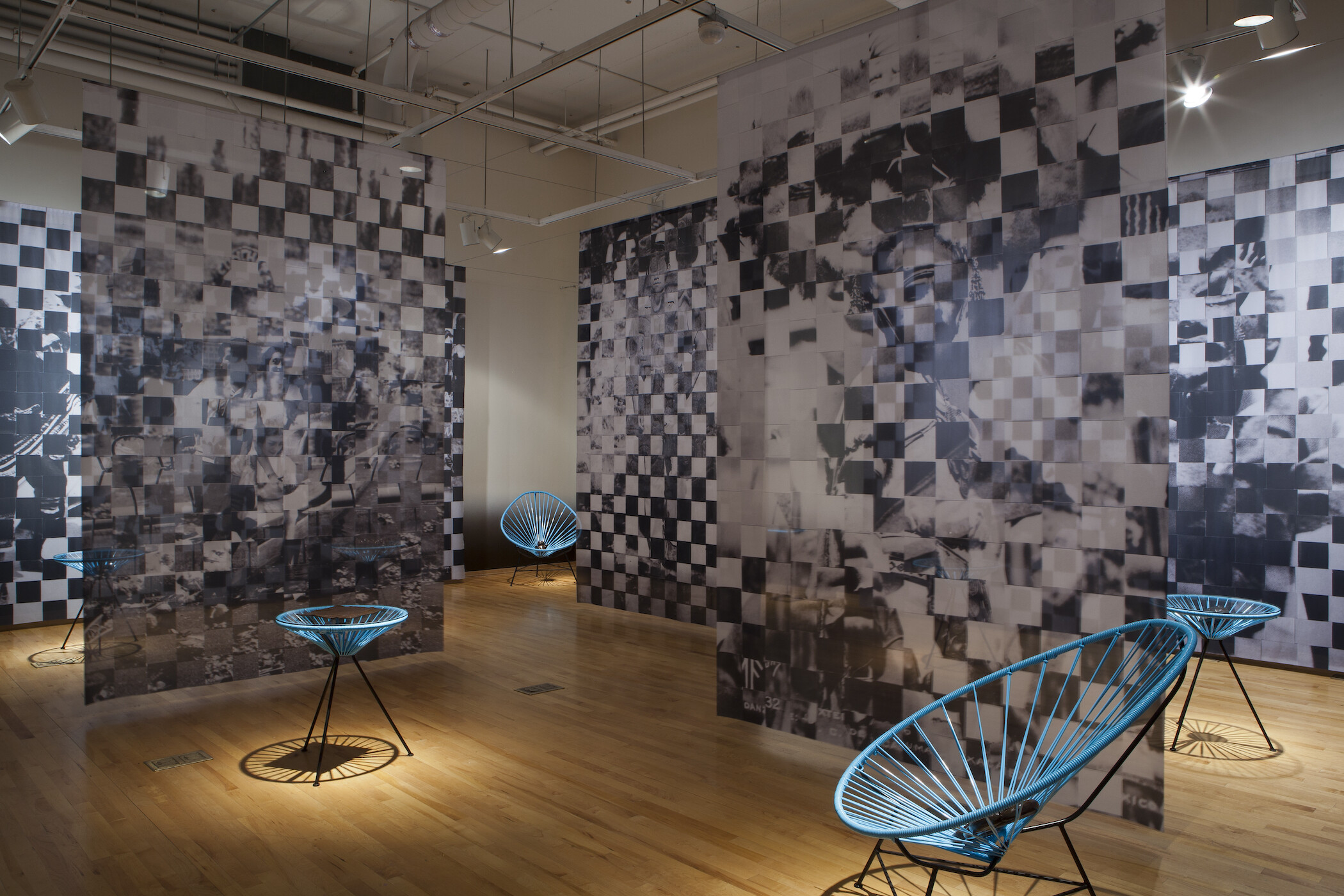 Gallery photo of black and white pixelated images hanging from ceiling and blue netted chairs holding black objects
