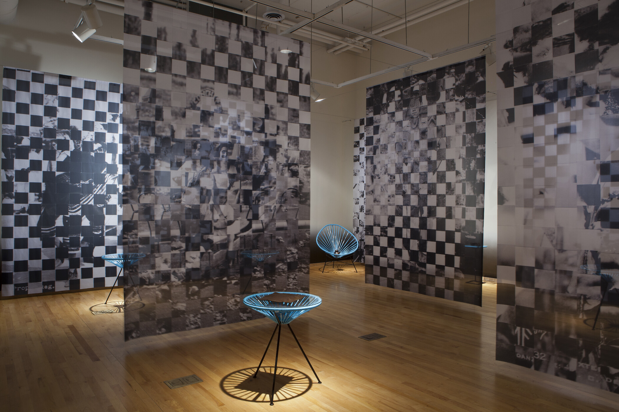 Gallery photo of black and white pixelated images hanging from ceiling and blue netted chairs holding black objects