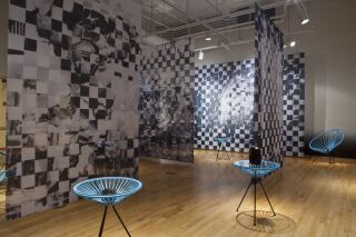 Gallery photo of black and white pixelated images hanging from ceiling and blue netted chairs holding black objects