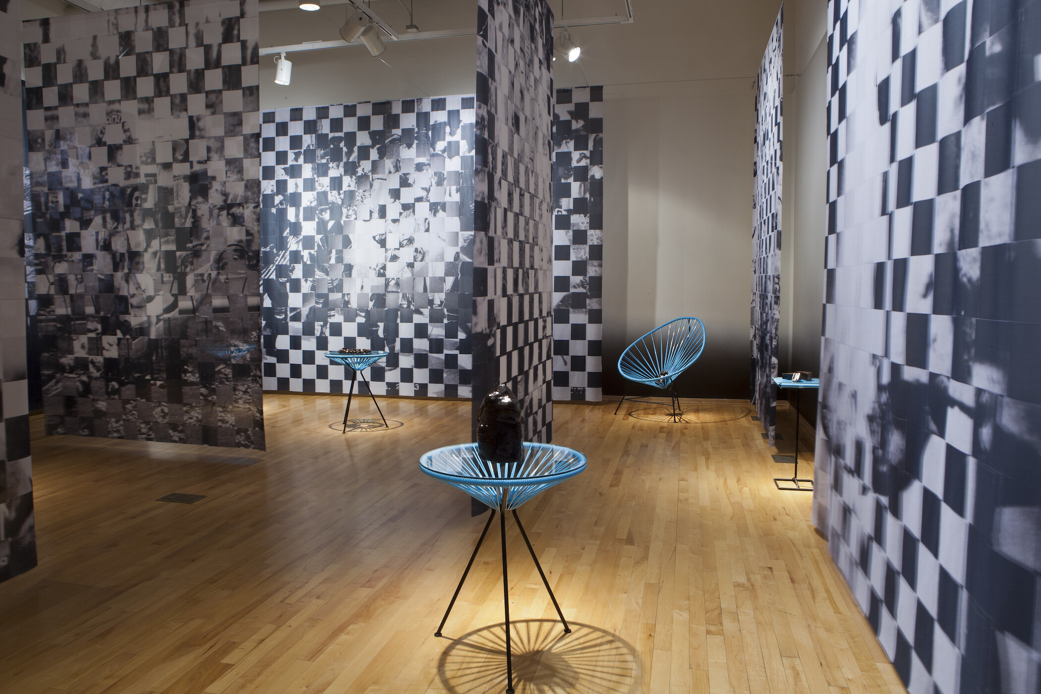 Gallery photo of black and white pixelated images hanging from ceiling and blue netted chairs holding black objects