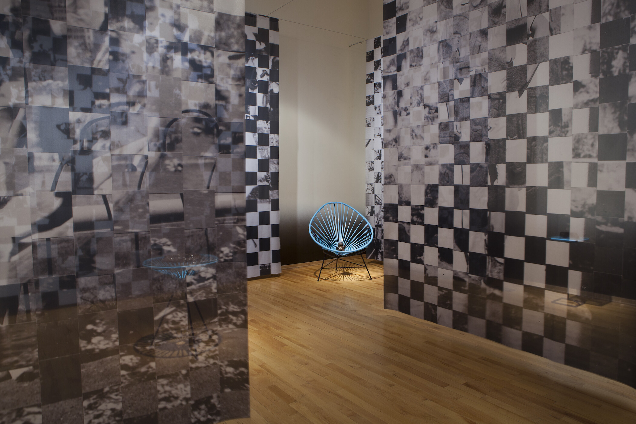 Gallery photo of black and white pixelated images hanging from ceiling and blue netted chairs holding black objects