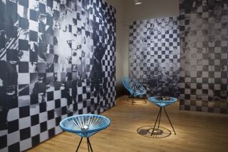 Gallery photo of black and white pixelated images hanging from ceiling and blue netted chairs holding black objects