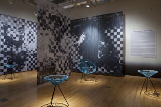 Gallery photo of black and white pixelated images hanging from ceiling and blue netted chairs holding black objects