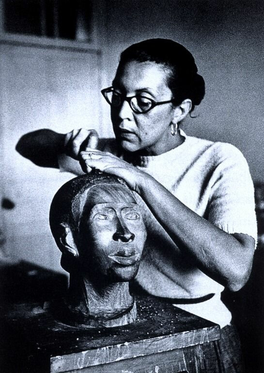 A woman with glasses carves the sculpture of a head