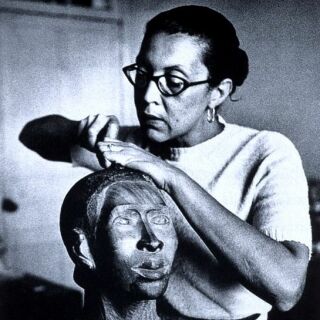 A woman with glasses carves the sculpture of a head