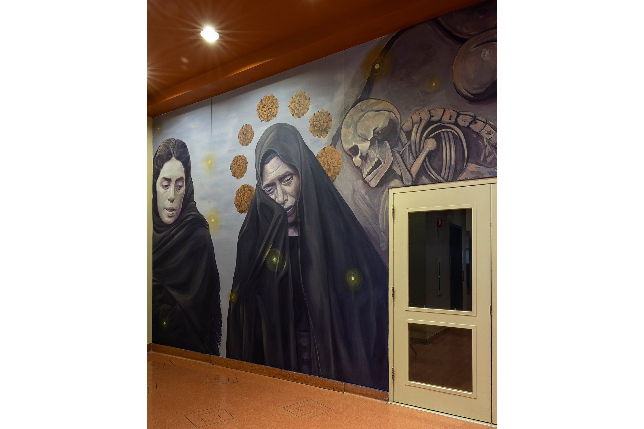 Two women dressed in all black mourning surrounded by yellow marigolds.