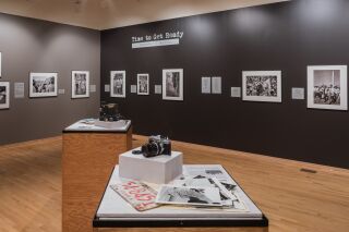 Photo of two gallery walls filled with black and white photos. Two podiums in the center of the room with cameras and paper documents