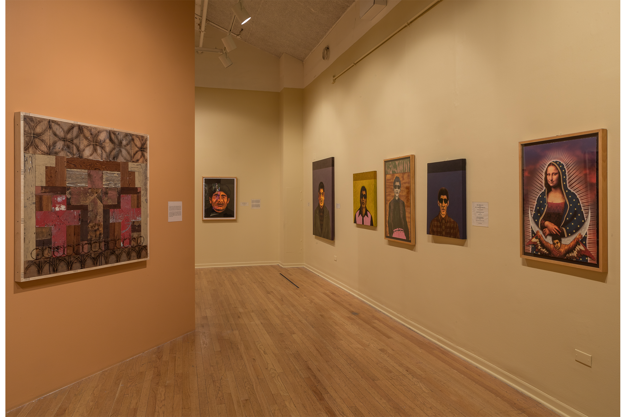 Seven artworks hang on a wall, one is created using lots of rectangular shapes, five are portraits of different men. The last, on the right, is a depiction of Holy Mary.