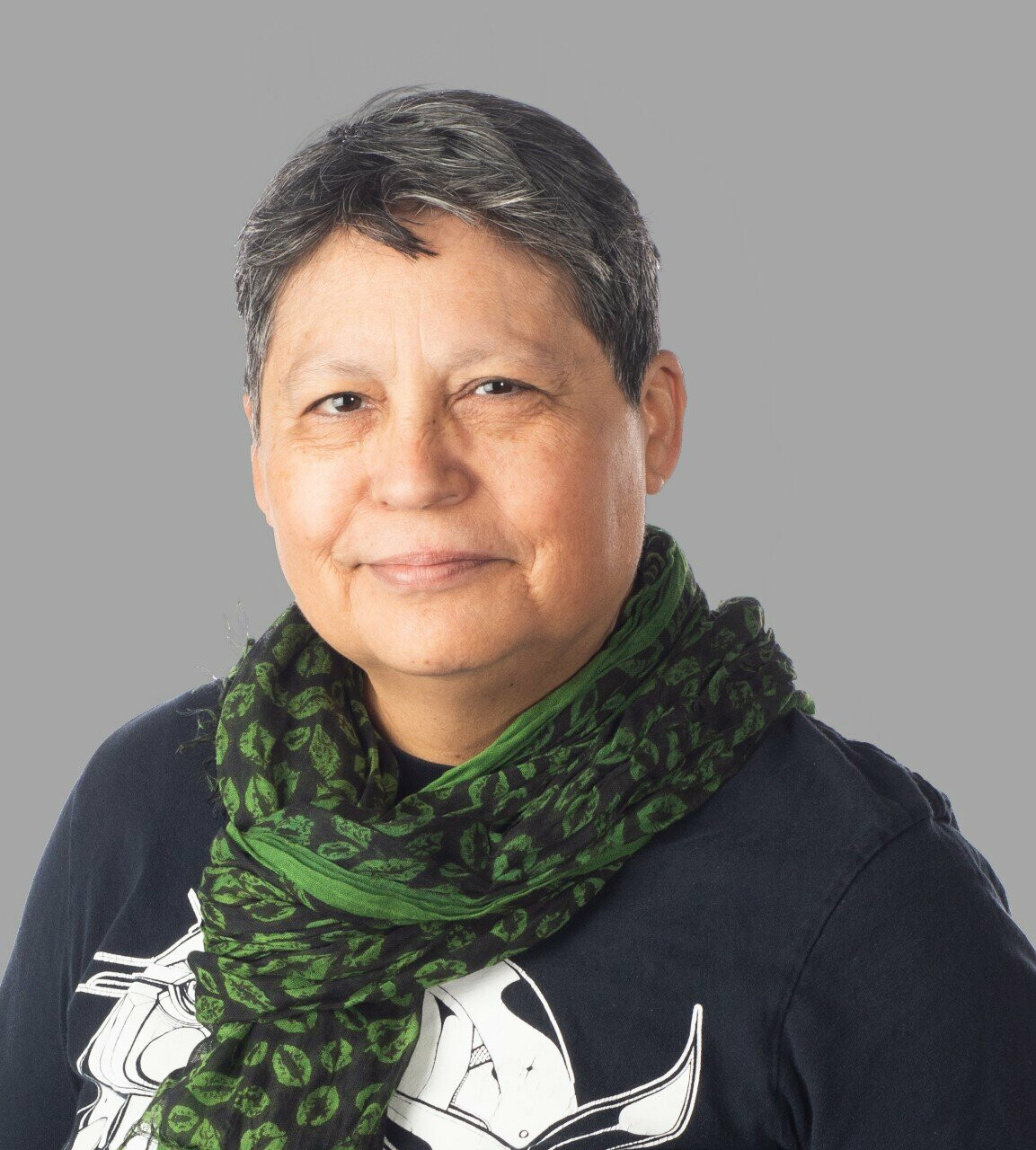 A person with short hair and a green scarf poses for a photo