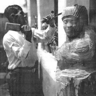 A man uses a chisel to carve a wooden sculpture