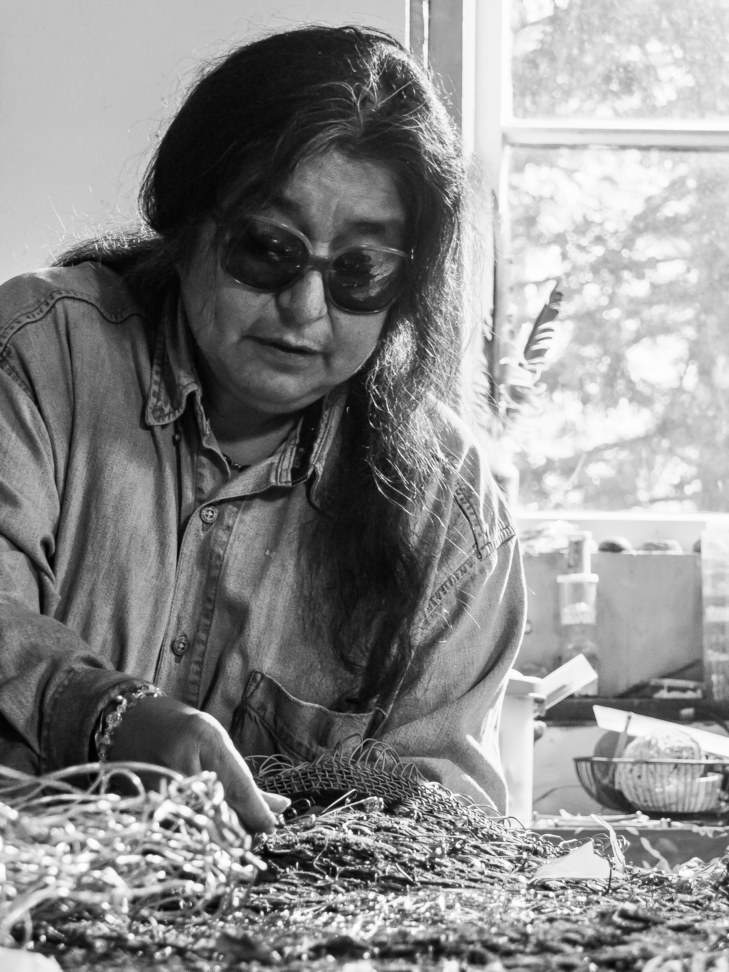 A person with long hair and dark glasses is working with textiles