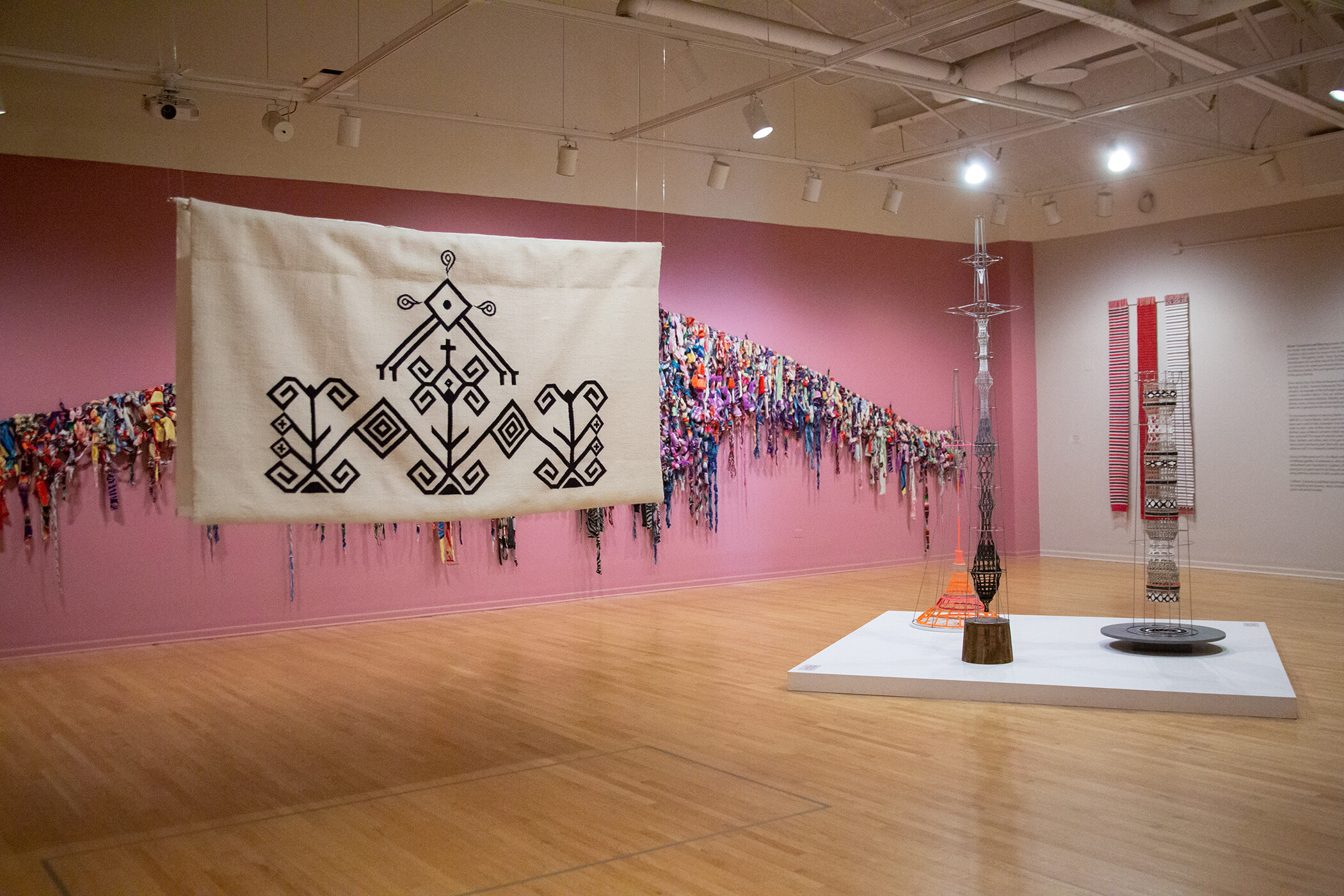 Wool canvas art piece hanging from ceiling on left side and three welded steel sculptures visible on right