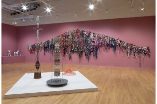 Gallery view with tall, thin welded sculptures in the center of the room and large weaving hung on wall
