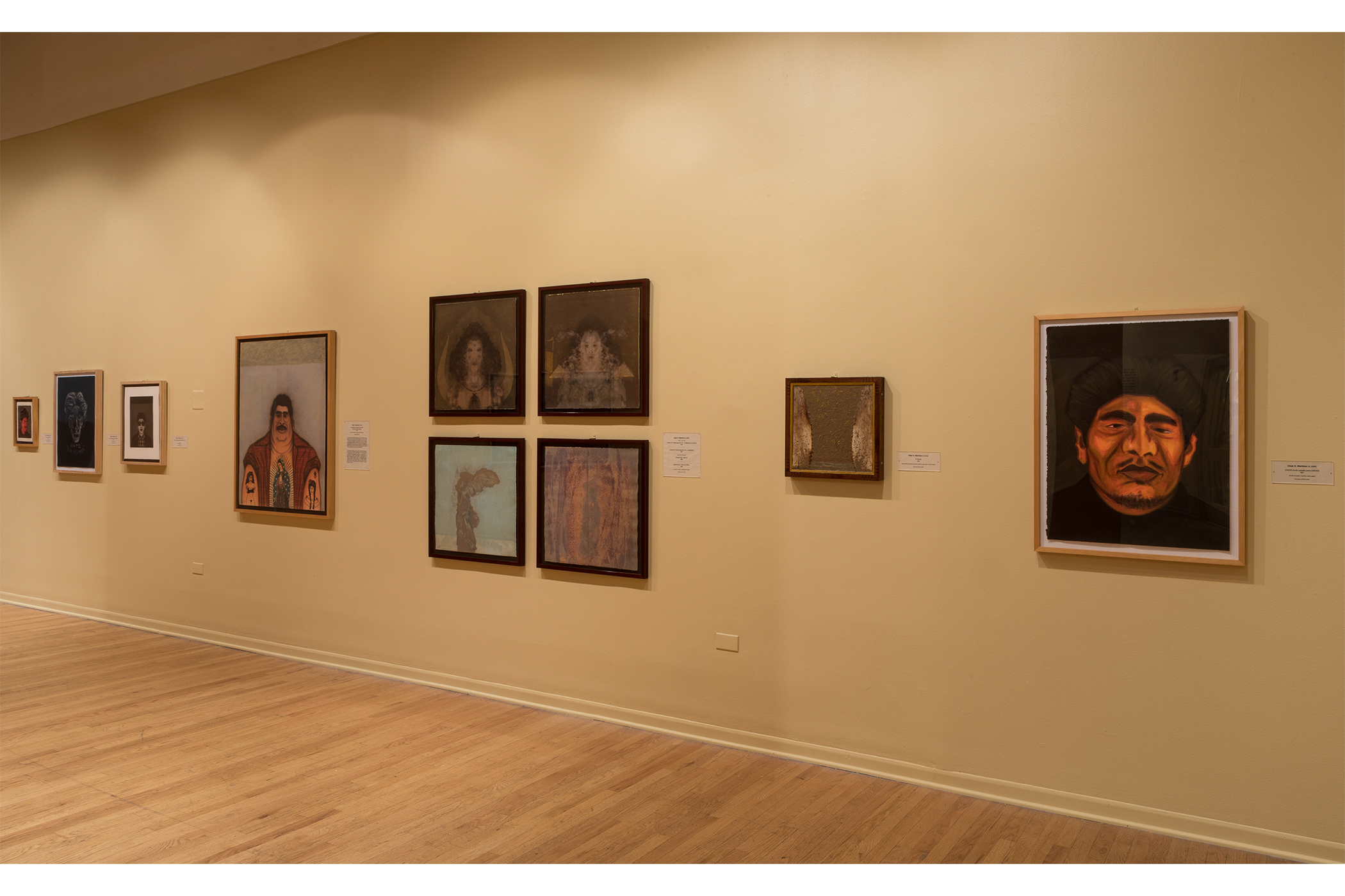 Ten different art pieces hanging on a beige wall in the gallery space.