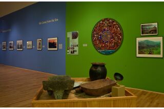 Long shot of one gallery walls split into two sections, with photographs, painting, and 3-D artifacts visible