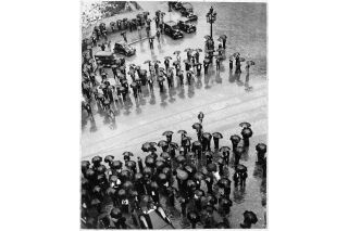 Black and white photo shot from above of large group of people in the street with black umbrellas