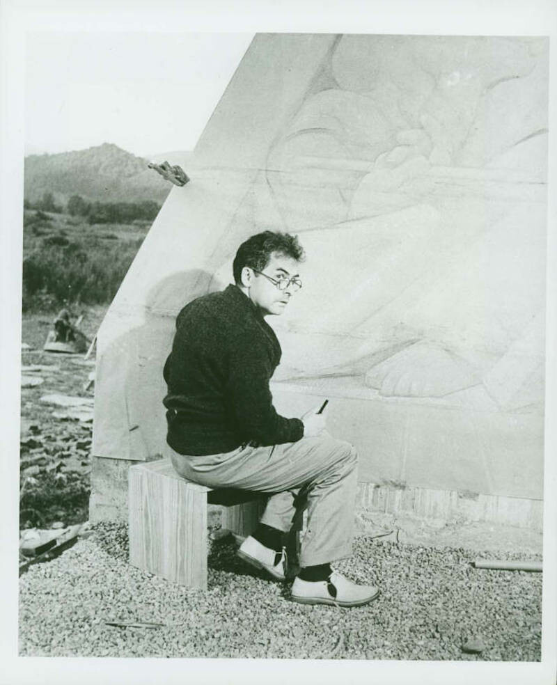 A seated man with his back toward the viewer turns his head