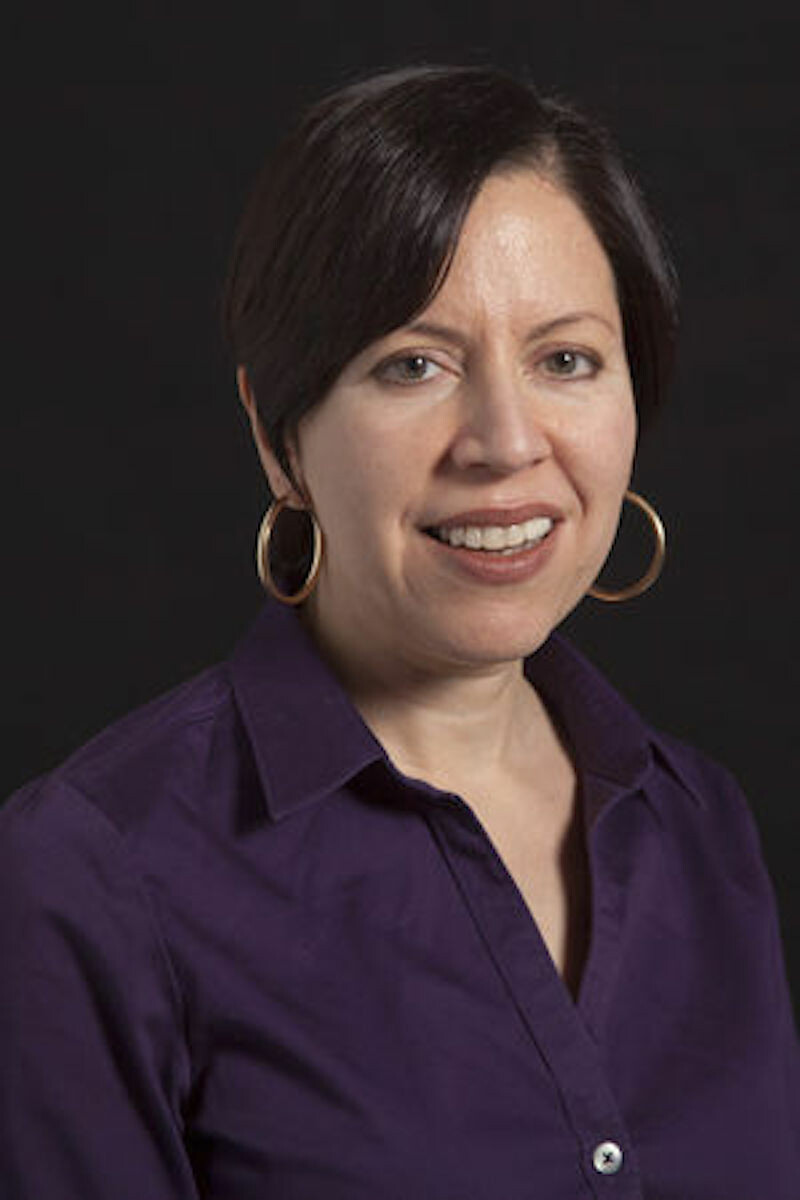 A woman with dark hair and hoop earrings poses for a photo
