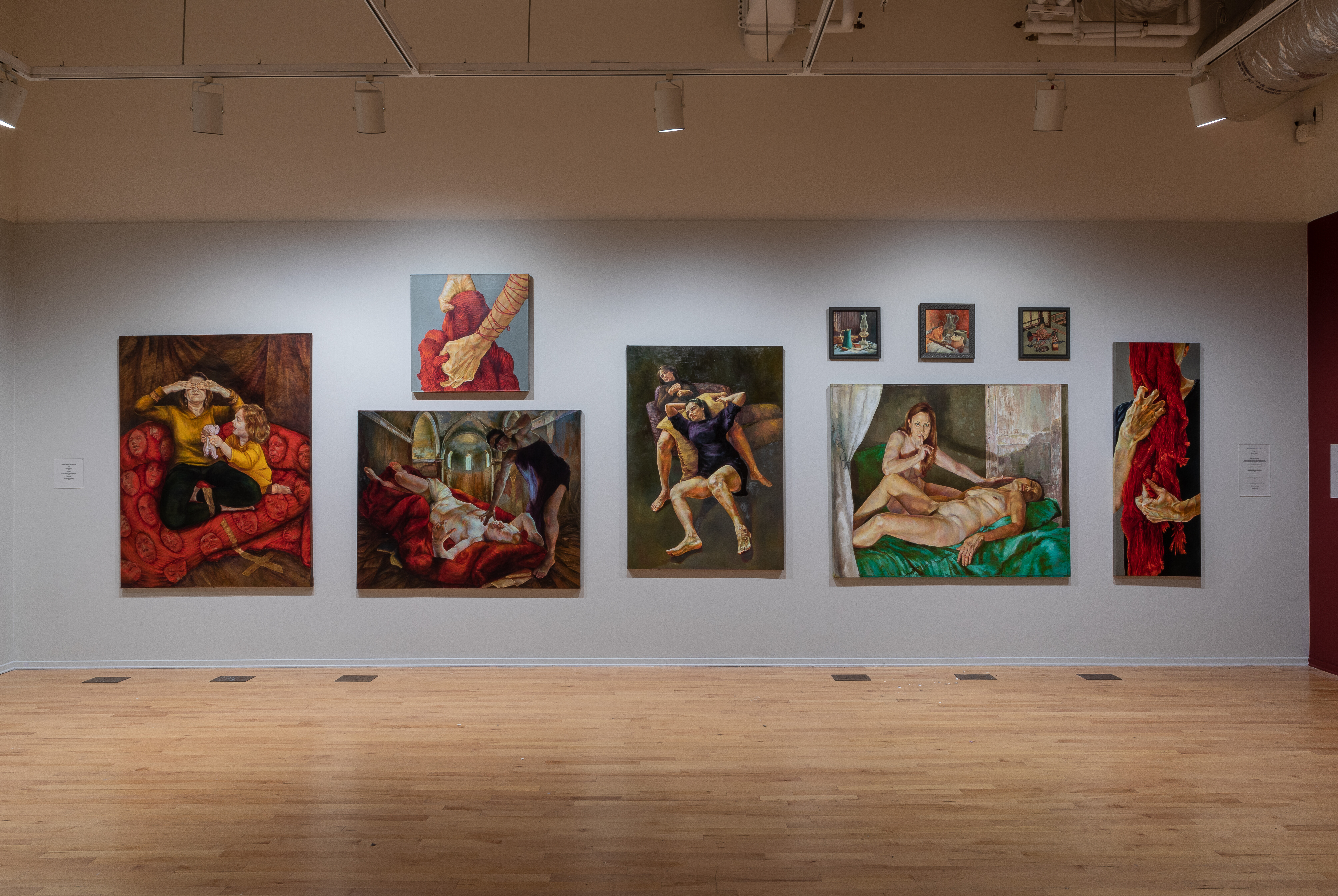 9 paintings in different sizes on light gray wall.