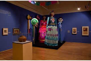 An installation of tall Street Puppets sit in the corner of the gallery.