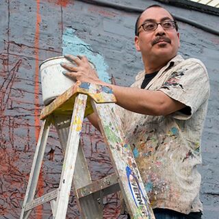 A man stands on a ladder and holds a bucket in front of a brick wall